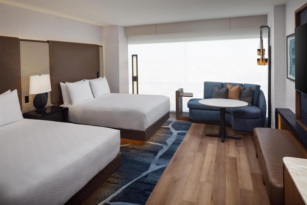 A hotel room with two beds, a sofa, a small table, and a TV.