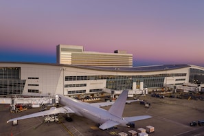 Un terminal d'aeroport amb un avió gran estacionat a la porta, una façana d'edifici corba i un cel serè.