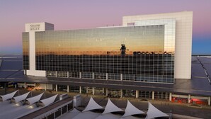 Un hotel moderno con fachada de vidrio, un letrero llamativo y un espacio al aire libre cubierto.