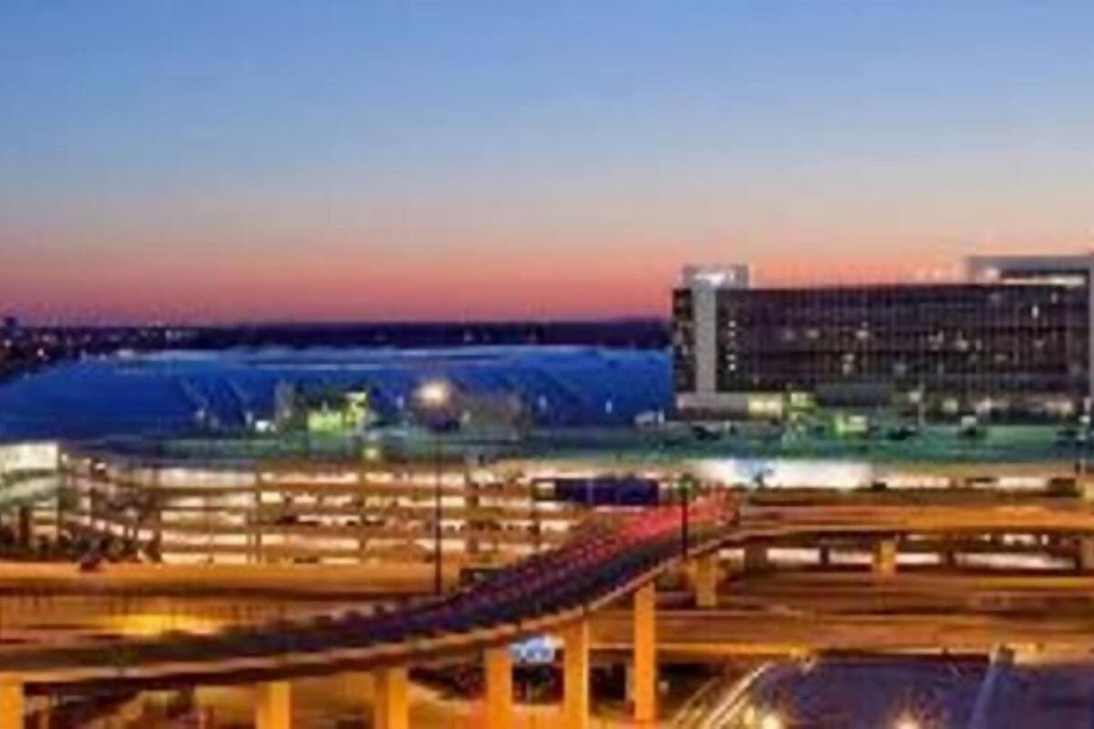 A modern building with a flat roof and large windows, surrounded by a parking area with multiple levels and a bridge.