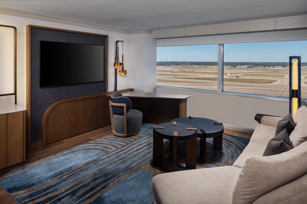 A modern hotel room with a large TV, a desk, a comfortable sofa, and a view of an airport.