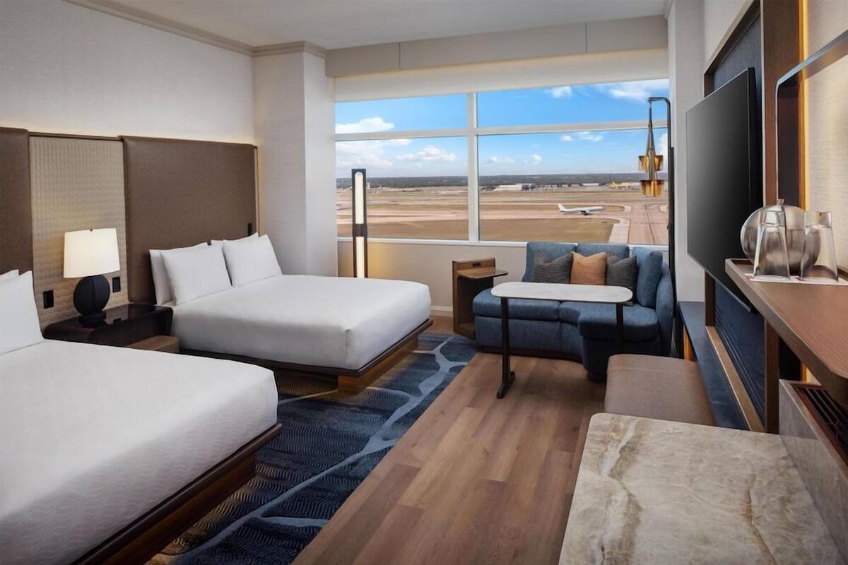 A hotel room with a bed, a sofa, a TV, and a view of an airport.