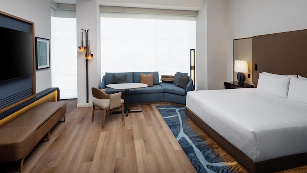 Habitación de hotel con cama, sofá, escritorio, televisor y ventana.