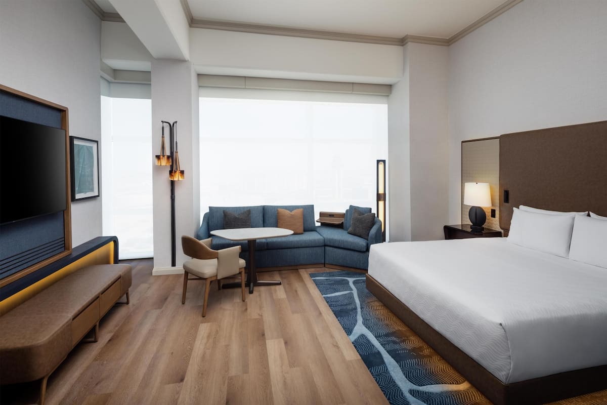 A hotel room with a bed, a sofa, a desk, a TV, and a window.