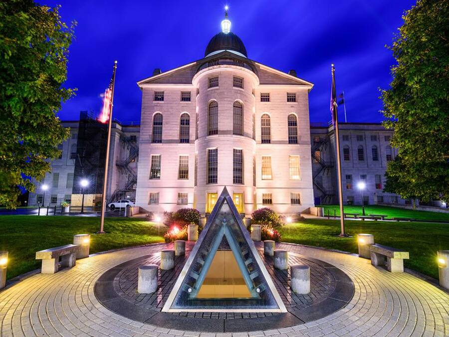 A large, historic building with a central courtyard featuring a triangular water feature, surrounded by a circular brick pathway and benches.