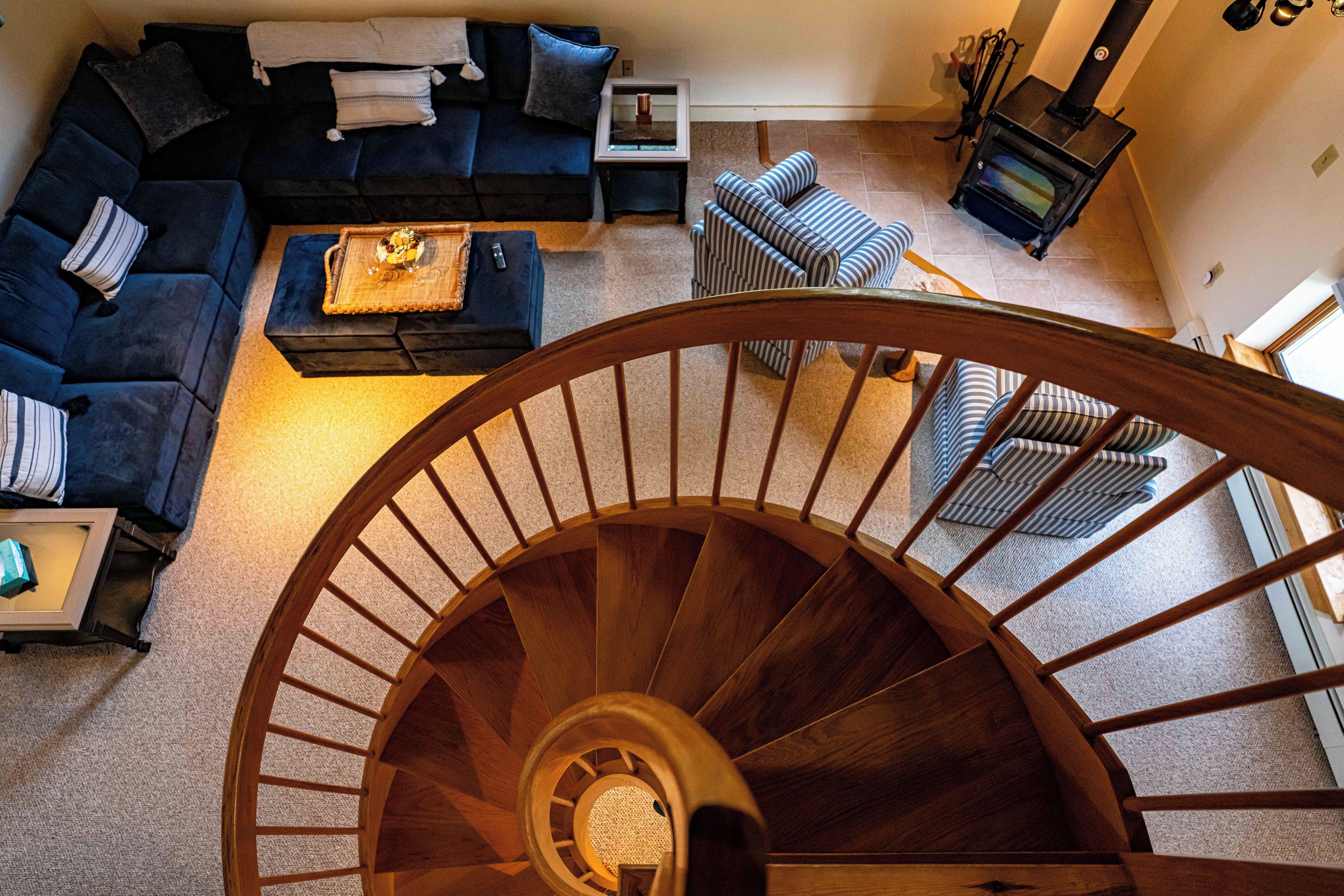 A spiral staircase in a living room with a blue sofa, a coffee table, and striped chairs.