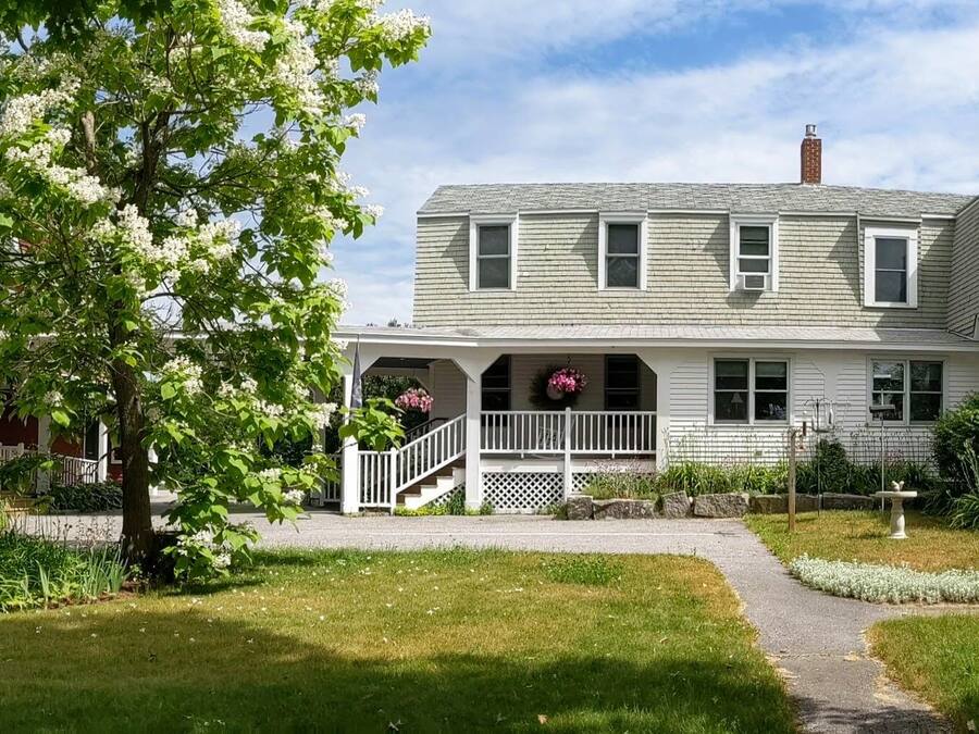 A two-story house with a green roof, a porch with a white railing, and a garden with a birdbath.