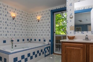 A bathroom with a bathtub, a wooden vanity, and a window with a view of greenery.