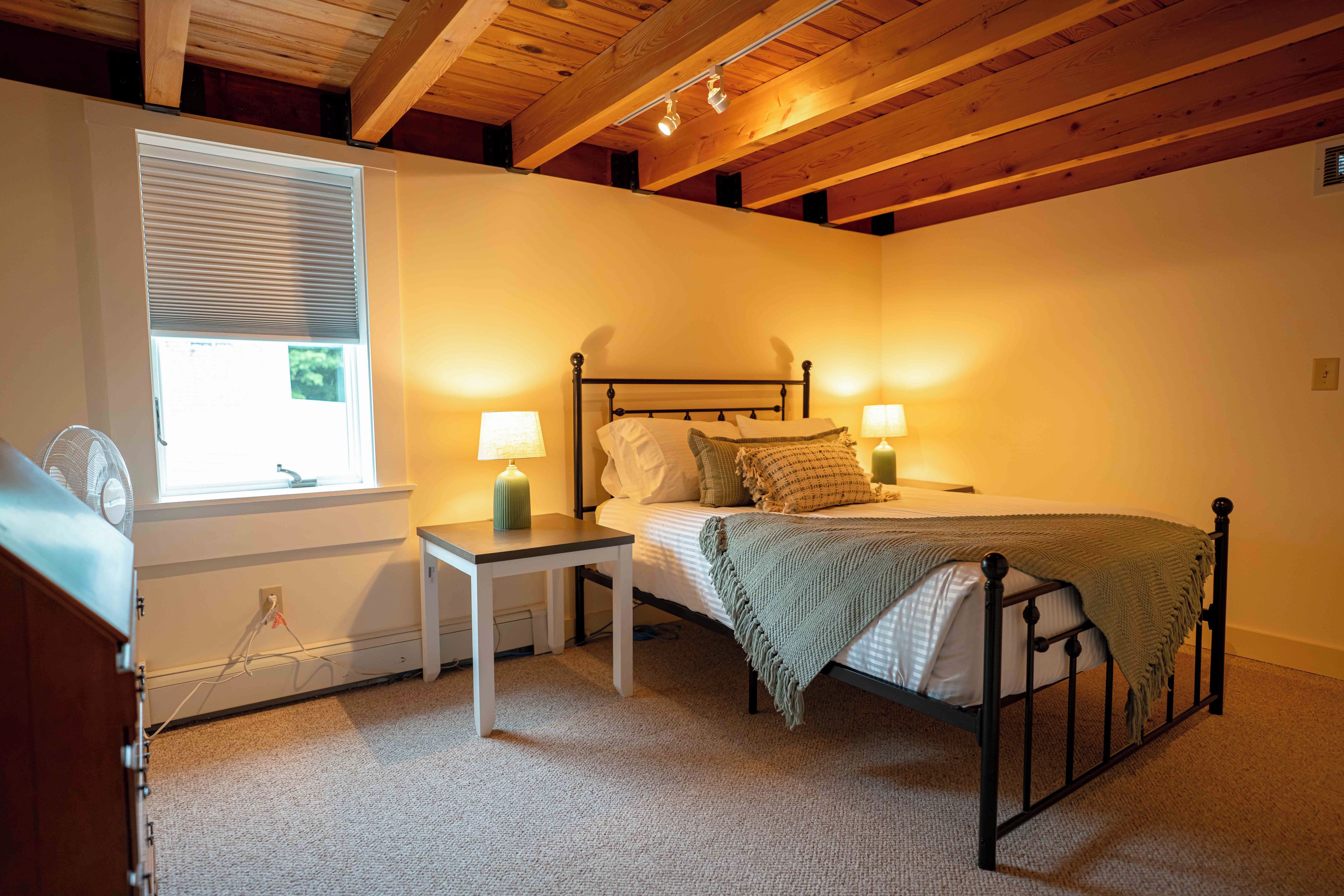 A bedroom with a bed, bedside lamps, a window with blinds, and a fan.