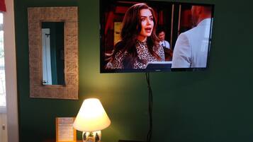 A television mounted on a wall, a lamp on a table, and a decorative mirror.