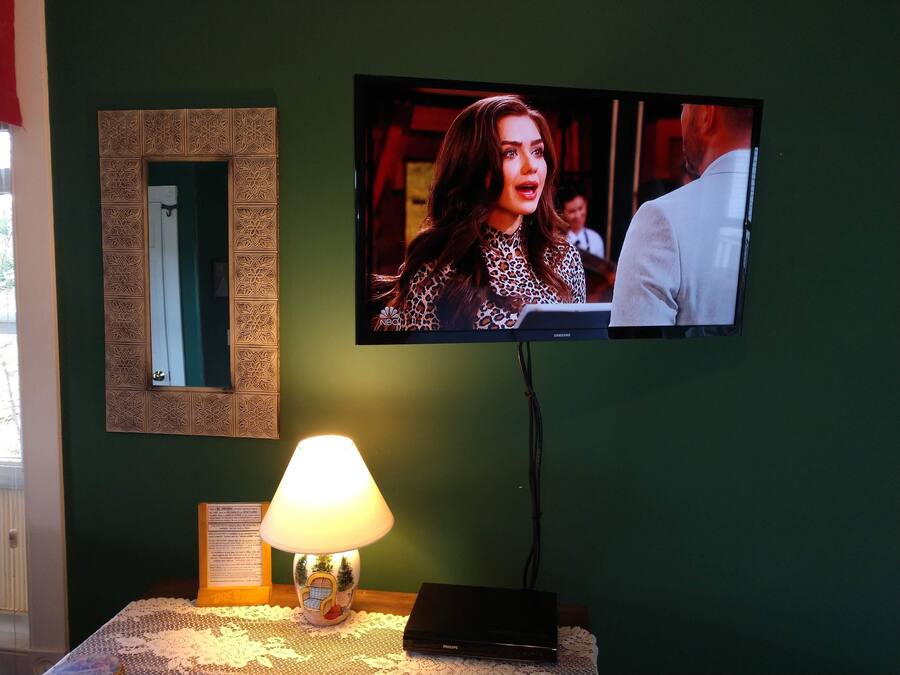 A television mounted on a wall, a lamp on a table, and a decorative mirror.