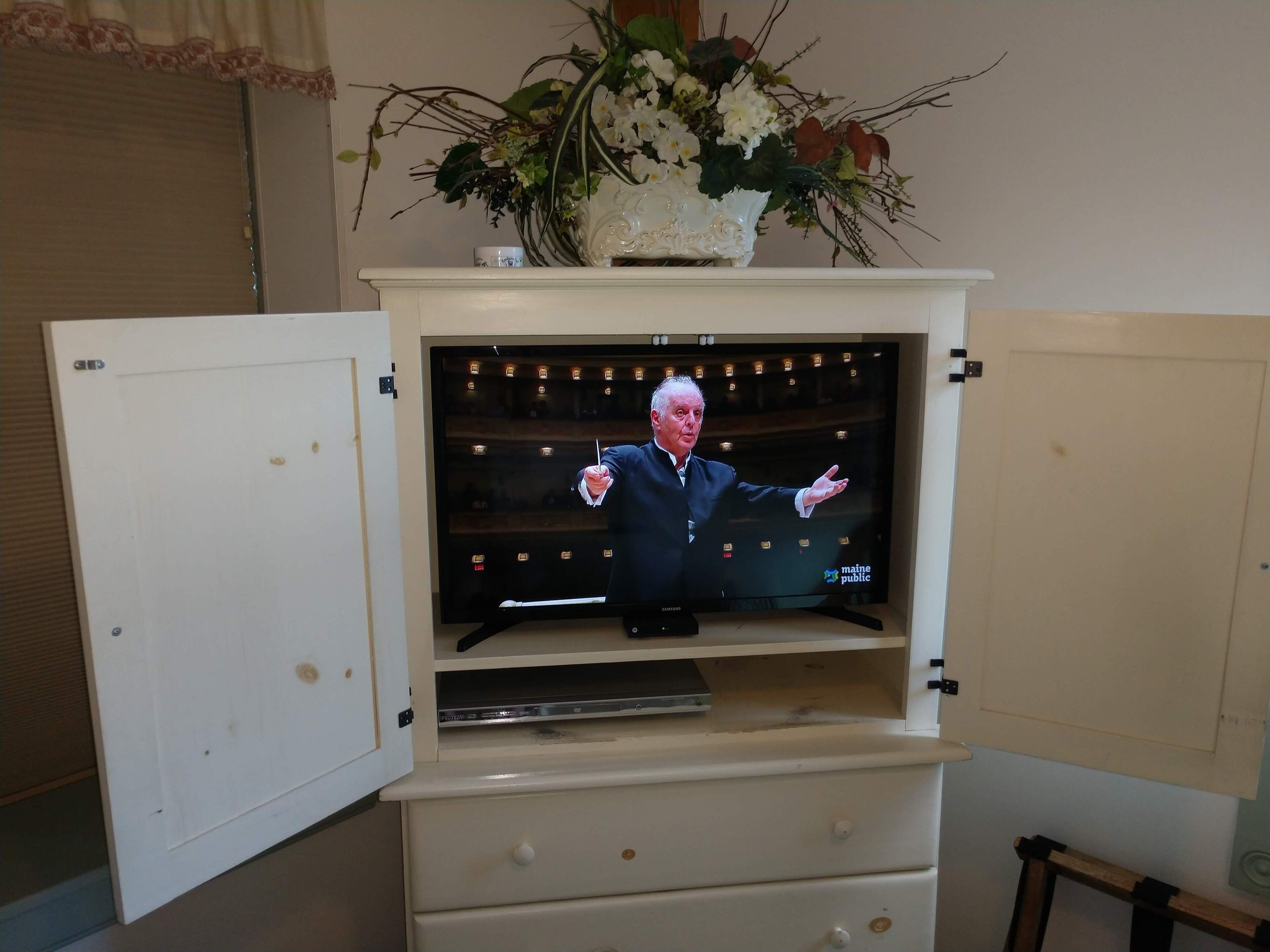 A television in a cabinet with a floral arrangement above it.