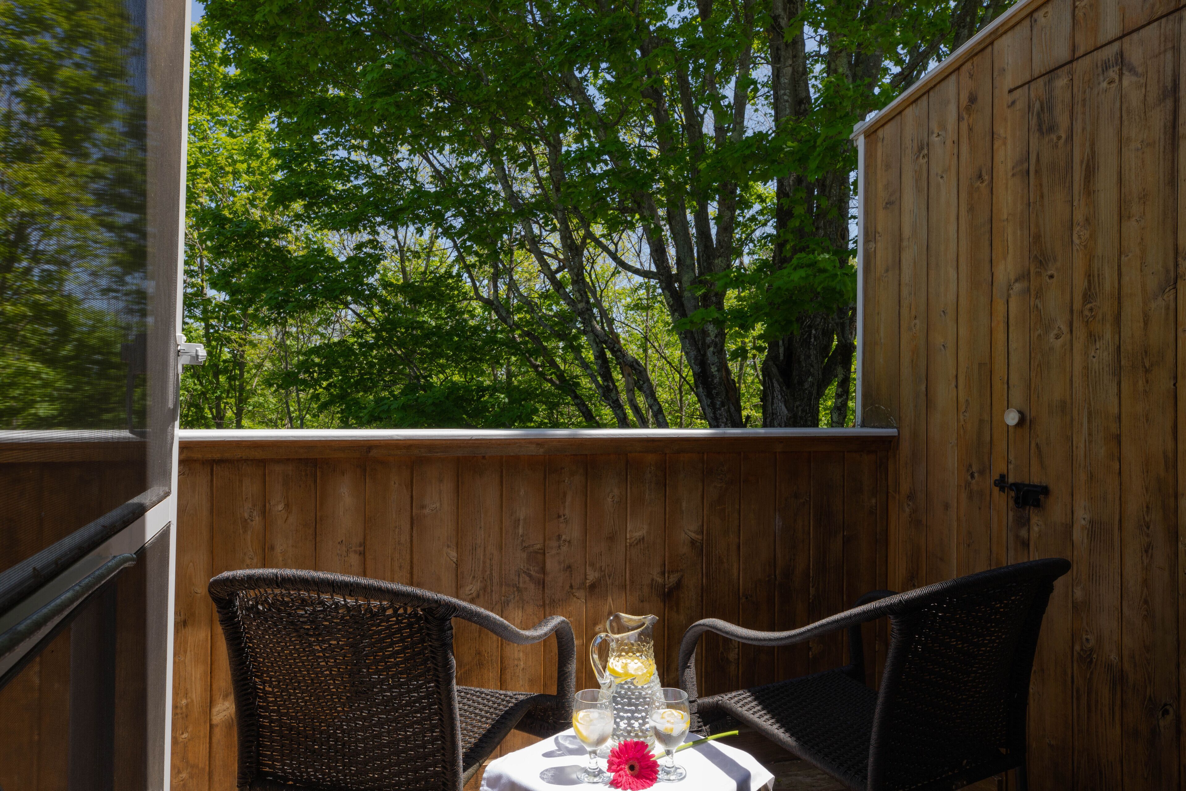 An outdoor patio with wicker chairs and a table set for two, featuring a pitcher and glasses.