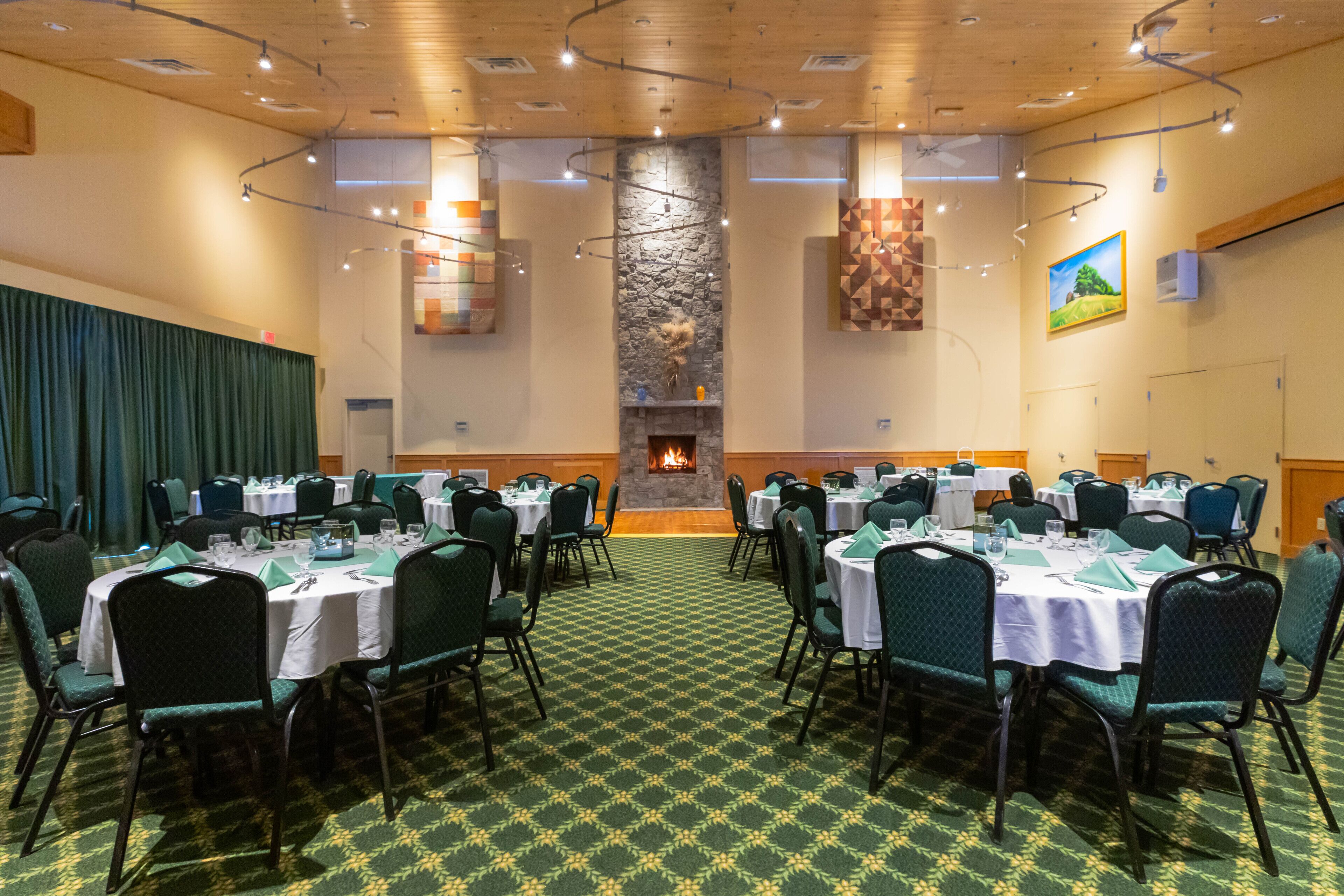 A conference room with round tables, green chairs, a stone fireplace, and a patterned carpet.