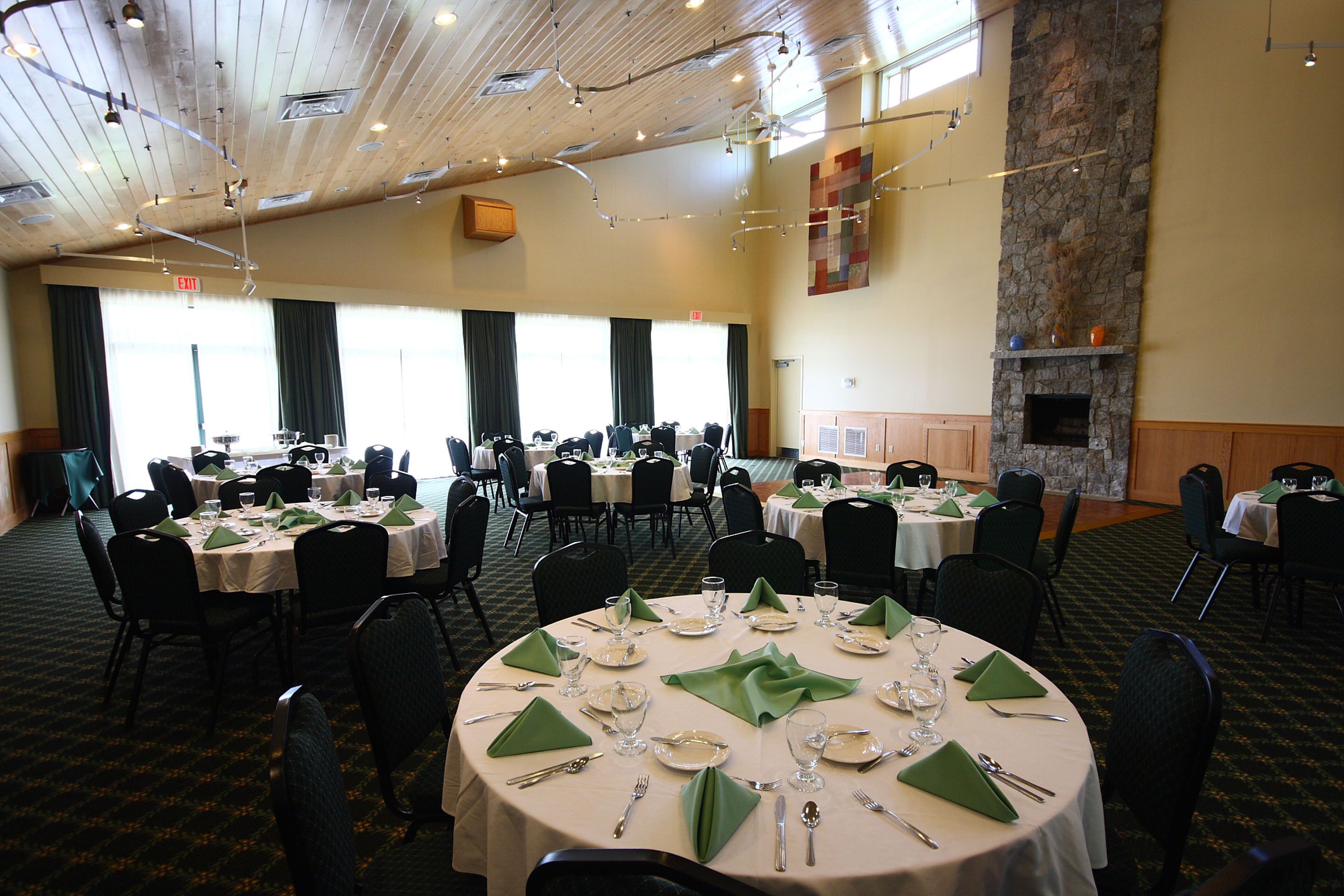 A banquet hall with multiple round tables set for dining, featuring green napkins and silverware.