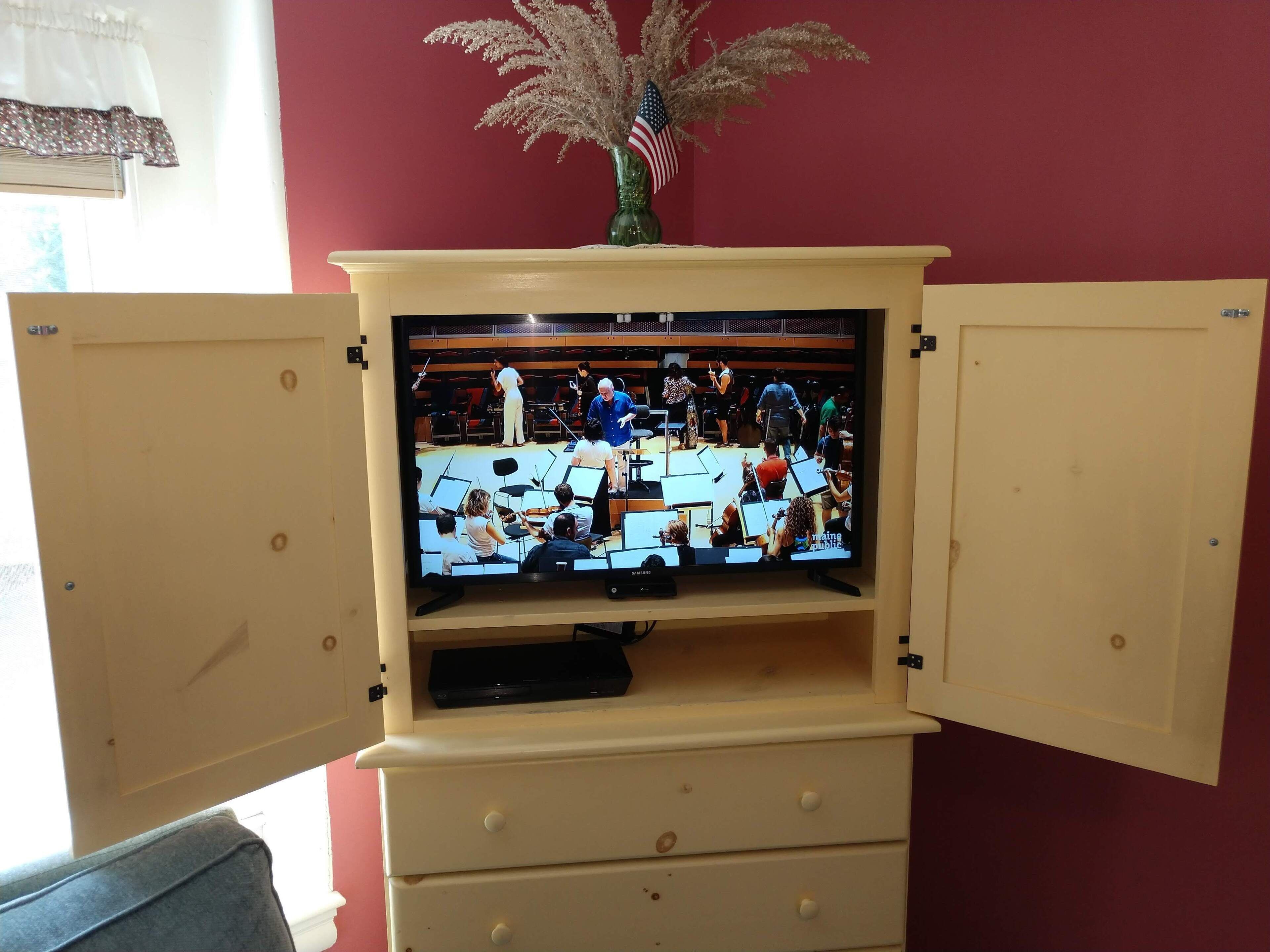 A television on a wooden cabinet with a red wall in the background.