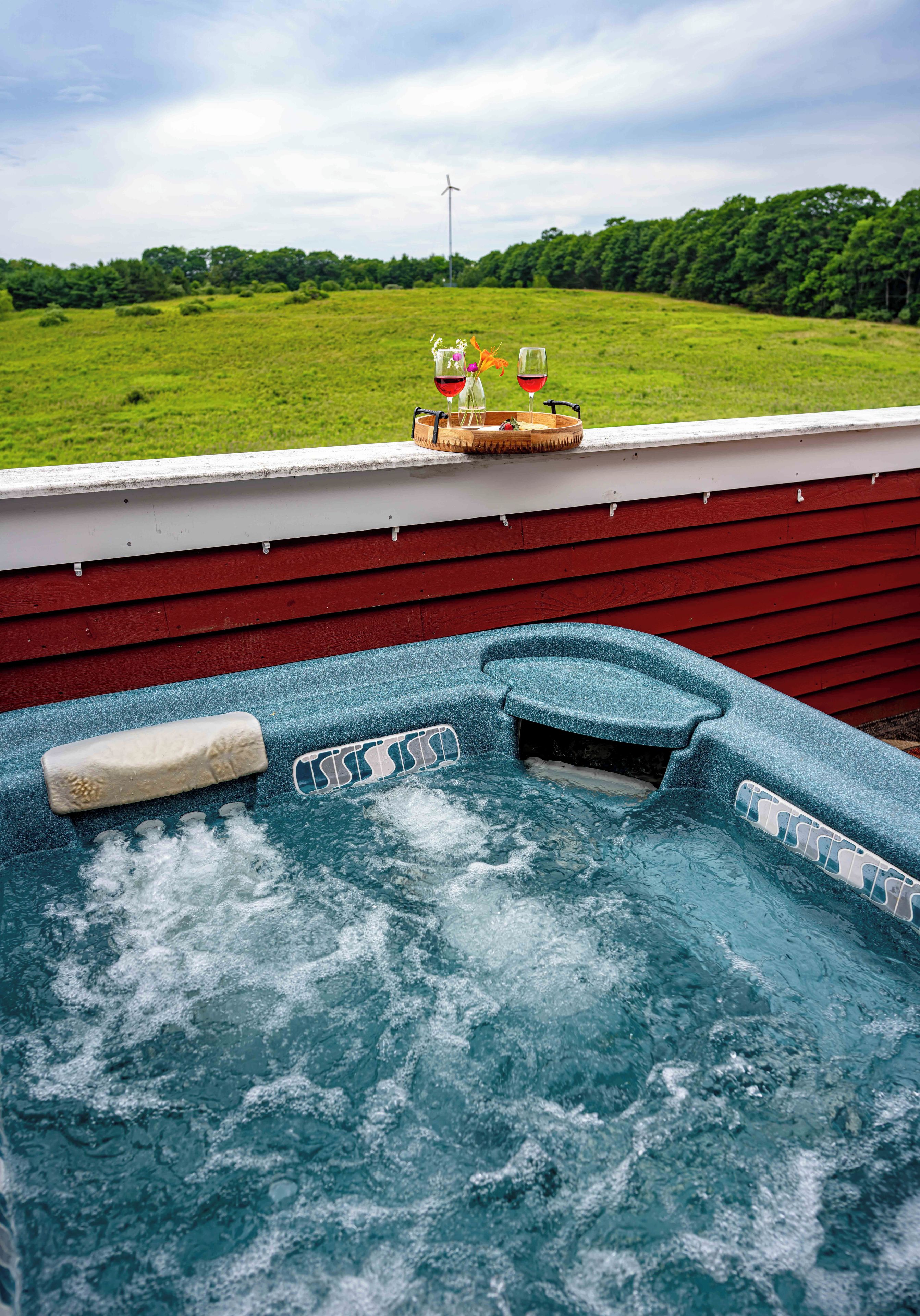 A hot tub with a view of a green field and a wind turbine in the distance.