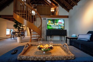A living room with a wicker tray holding snacks, a television displaying a program, and a staircase leading to an upper level.