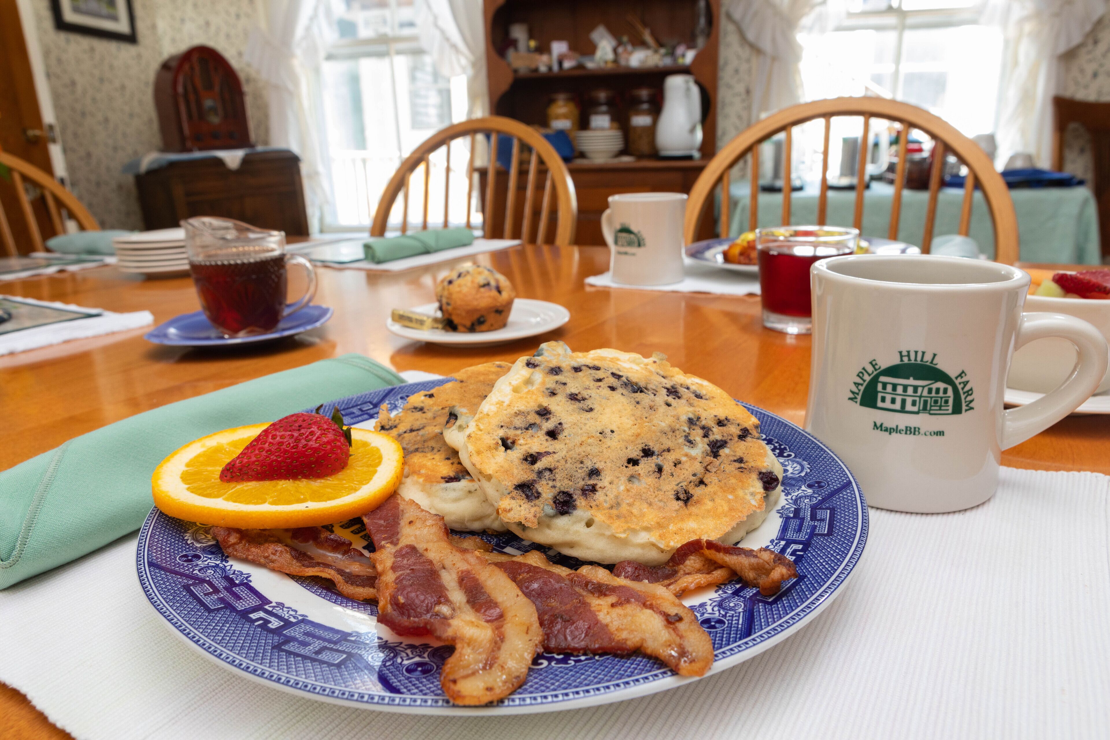En morgenmadstallerken med pandekager, bacon, en jordbær og en appelsinskive.