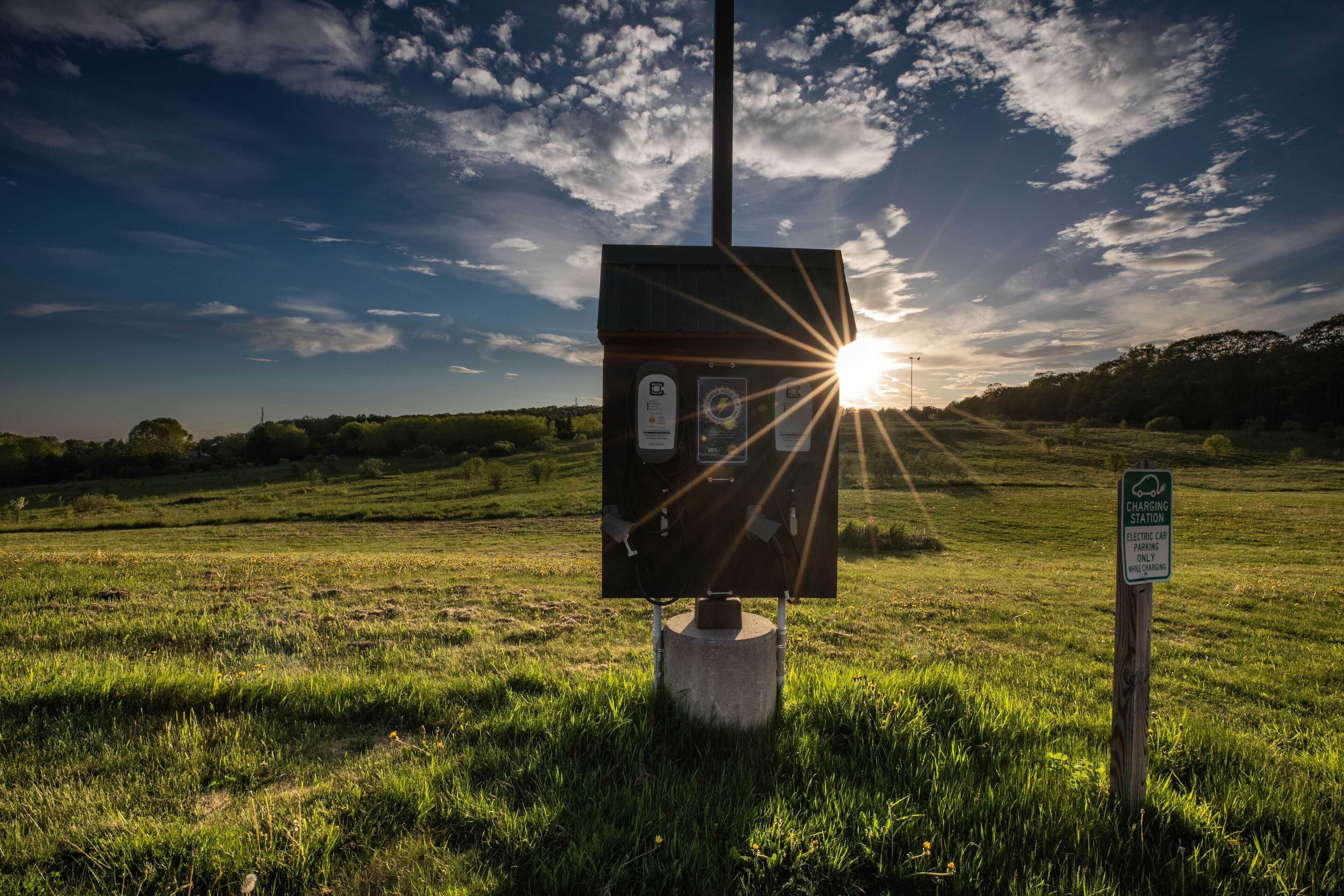A charging station in a grassy field with a clear sky and sun setting in the background.