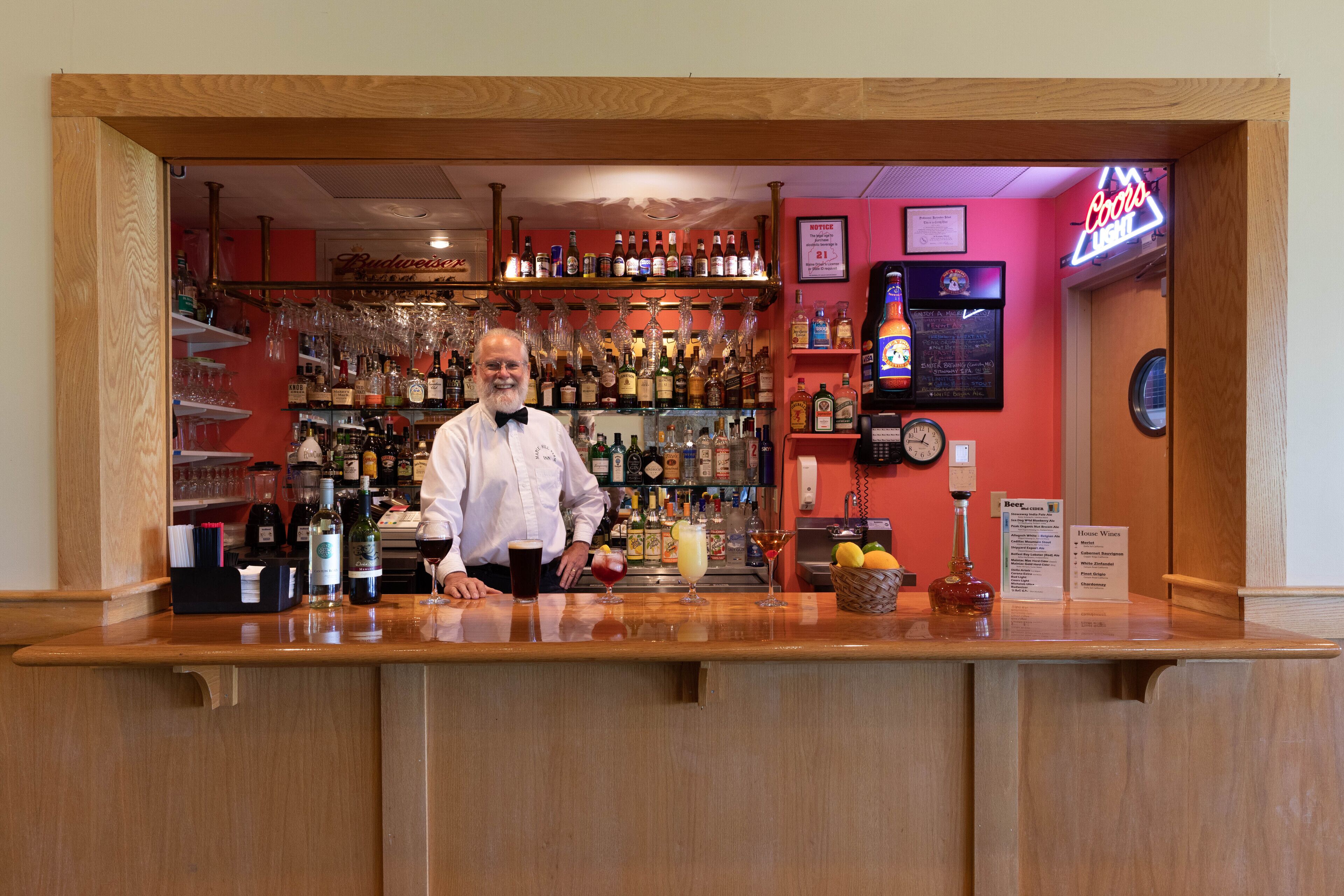 Un bar con mostrador de madera, estantes con botellas, vasos y un letrero de neón.