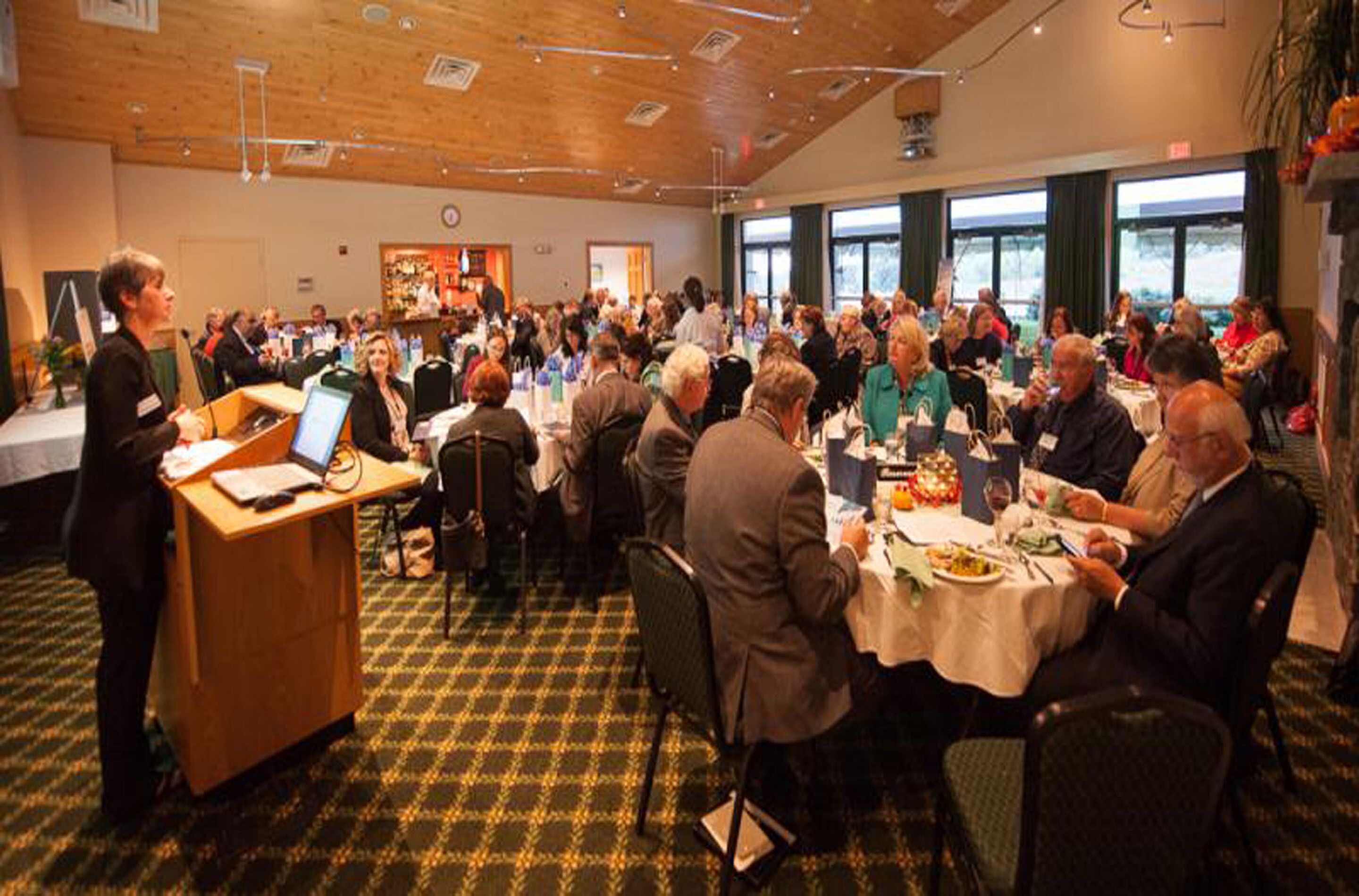 A conference room with round tables, attendees seated, and a speaker at the front.