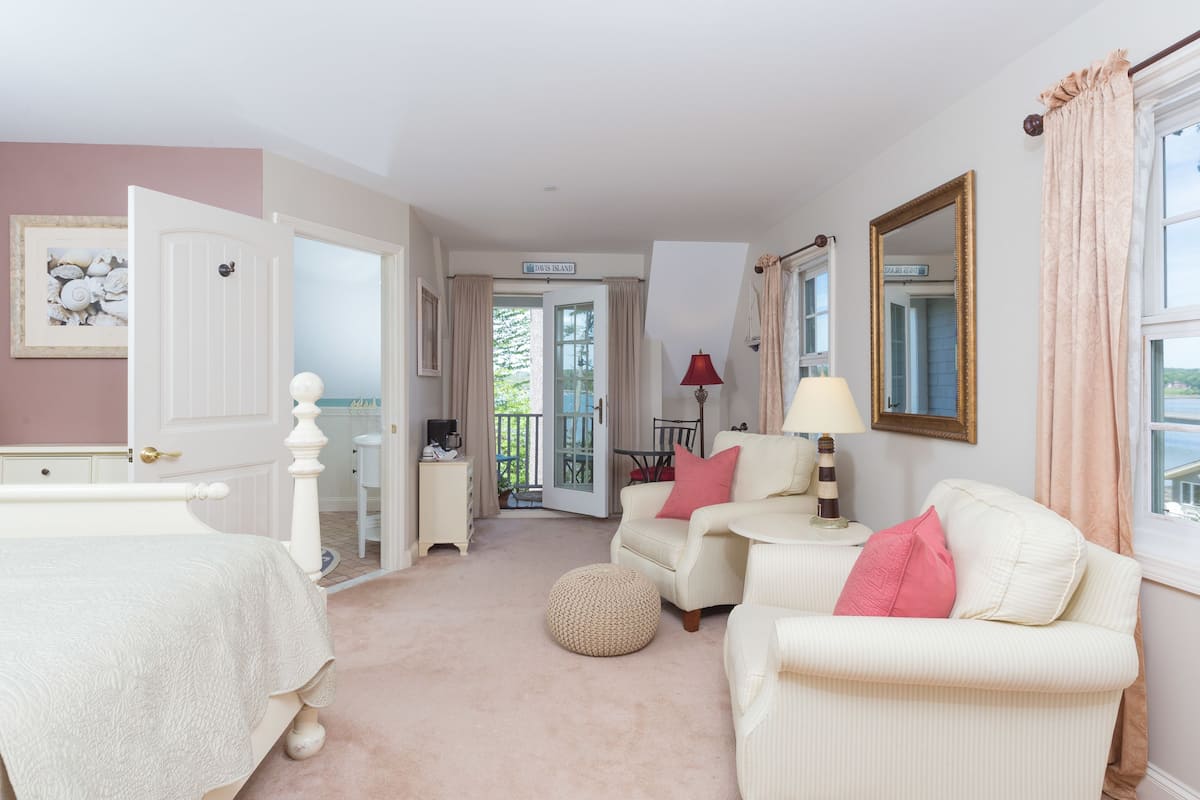 A room with a bed, two chairs, a table, a lamp, and a window with curtains.