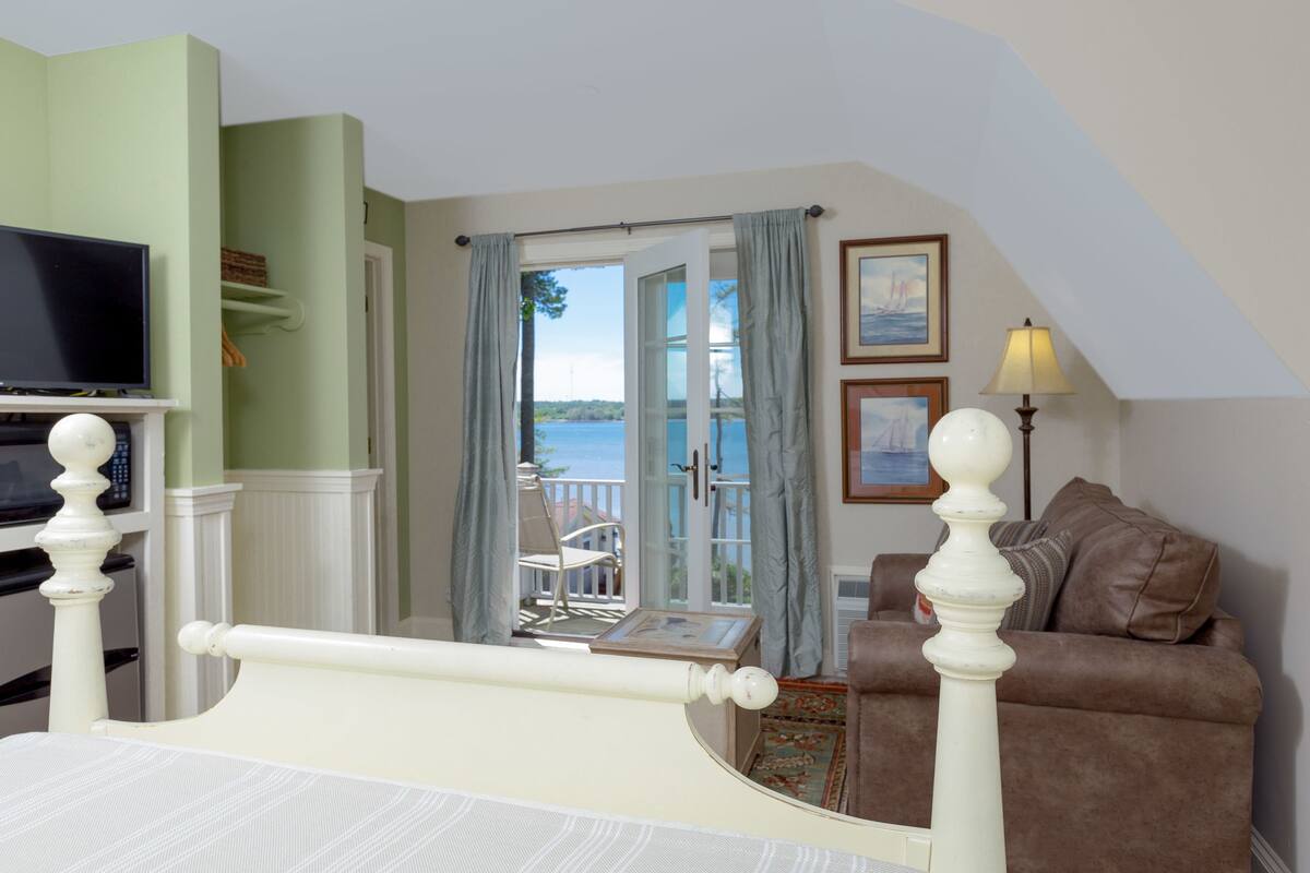 A bedroom with a bed, a television, a window with curtains, a balcony, and a sofa.