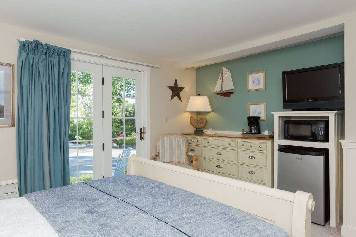 A bedroom with a bed, a dresser, a television, a microwave, and a refrigerator.