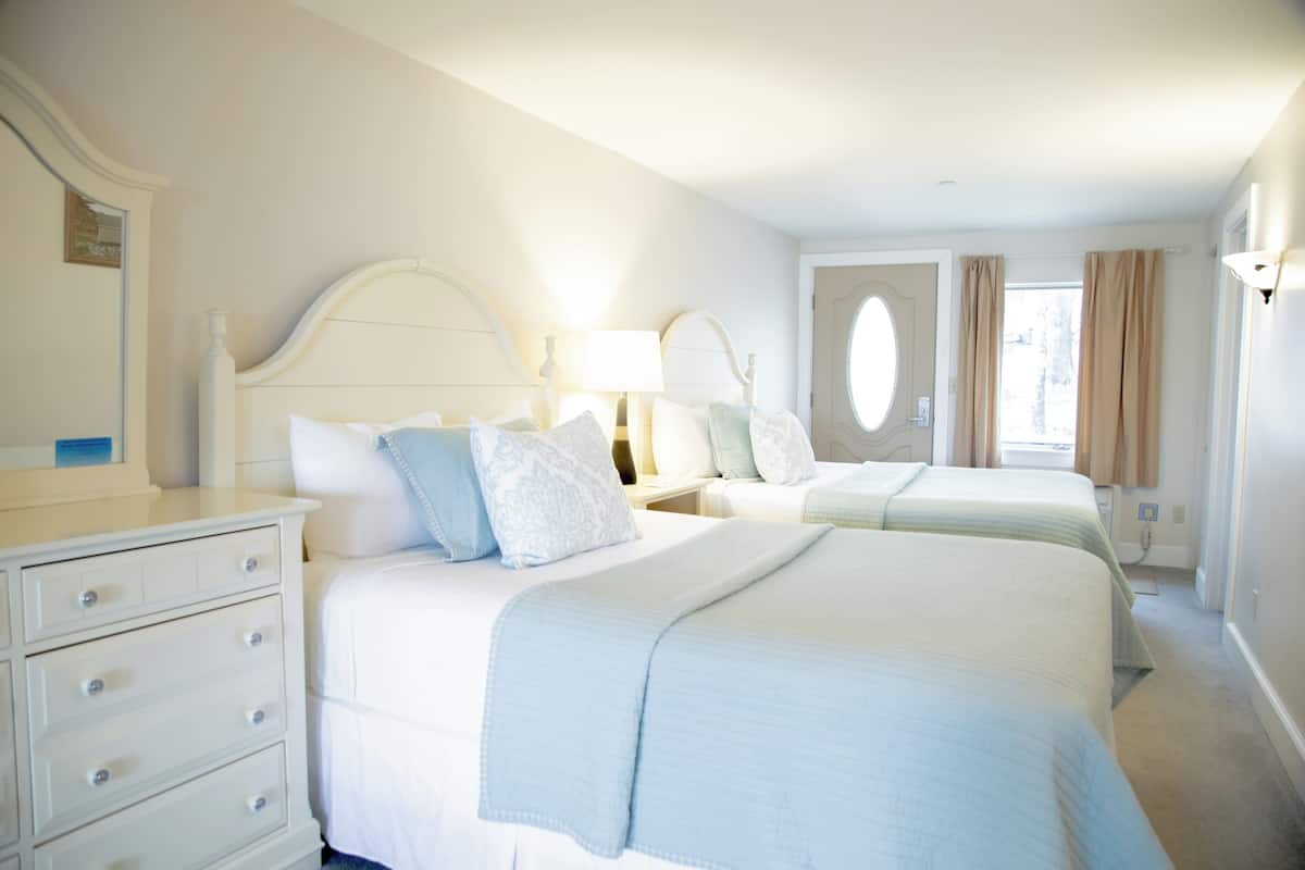 A hotel room with two beds, a dresser, and a window with curtains.