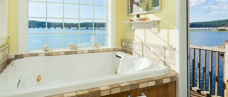 A bathroom with a large bathtub, a window with a view of a lake, and a wooden deck outside.