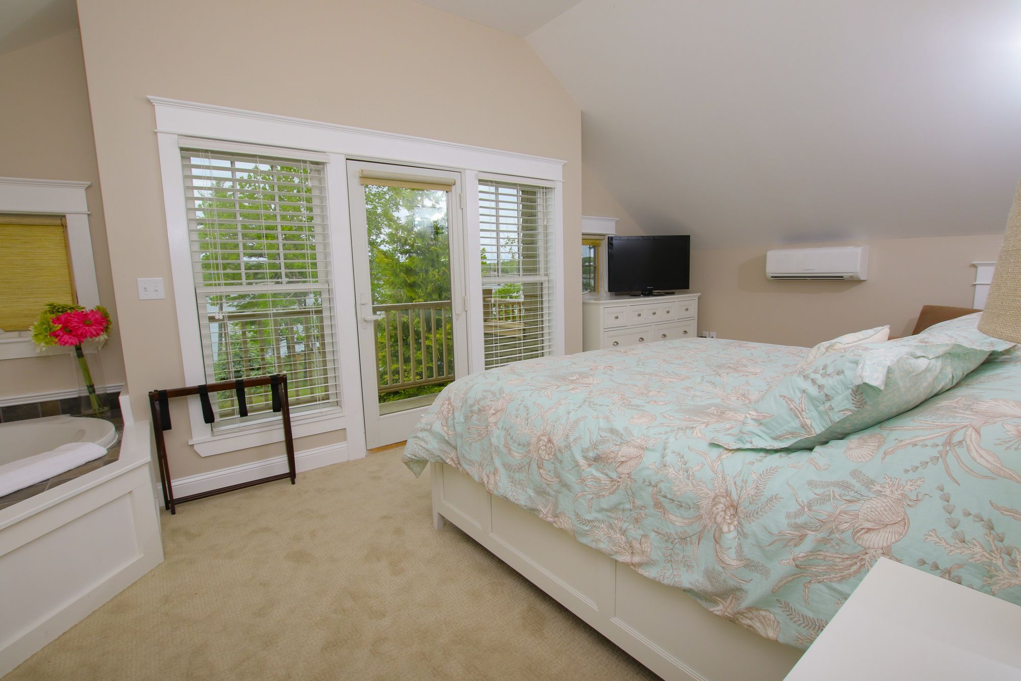 Une chambre à coucher comprenant un lit, une télévision, un climatiseur, une fenêtre avec des stores et une vue sur la verdure.