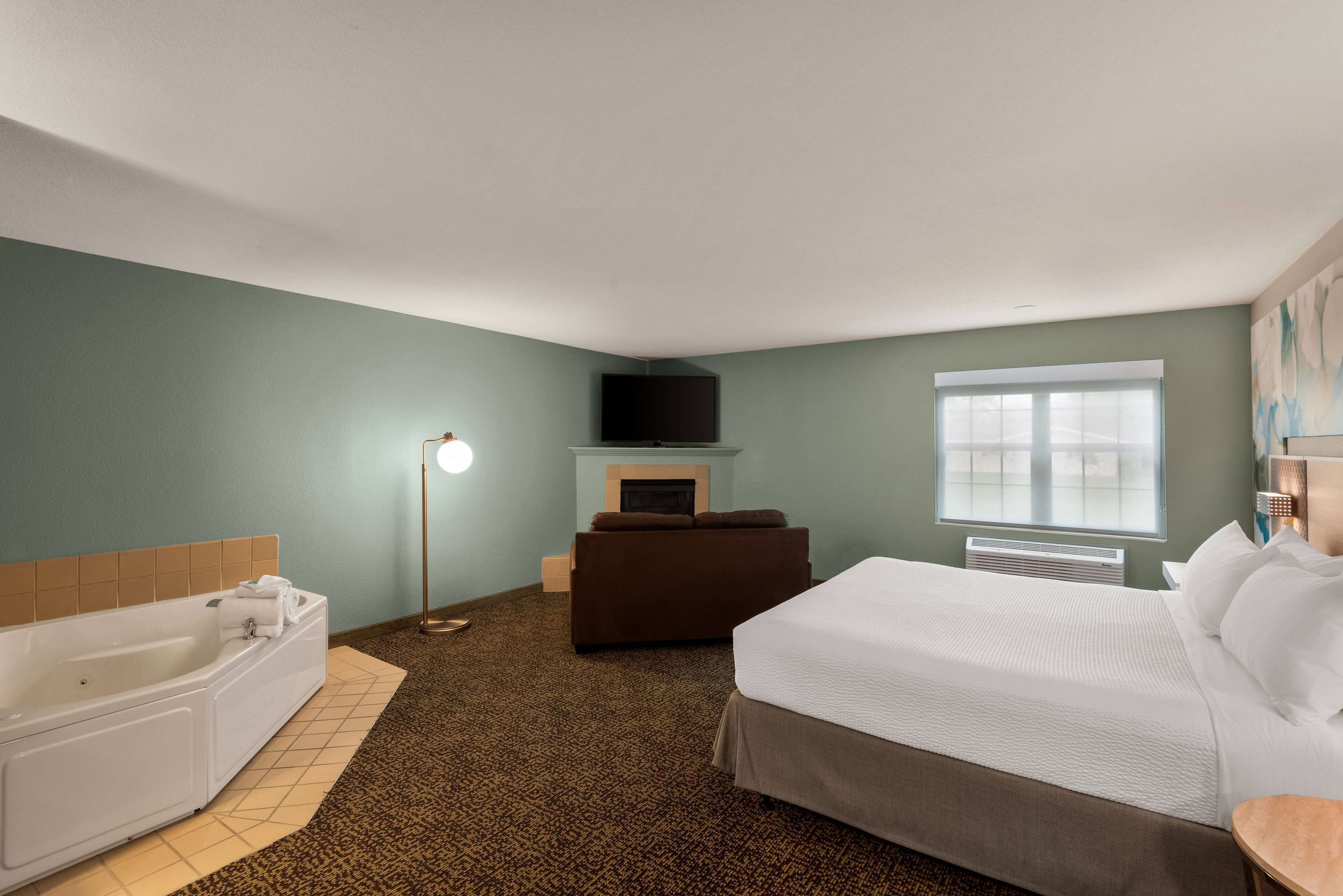 Ein Hotelzimmer mit einem großen Bett, einer Sitzecke, einem Flachbildfernseher, einem Kamin und einer Badewanne.