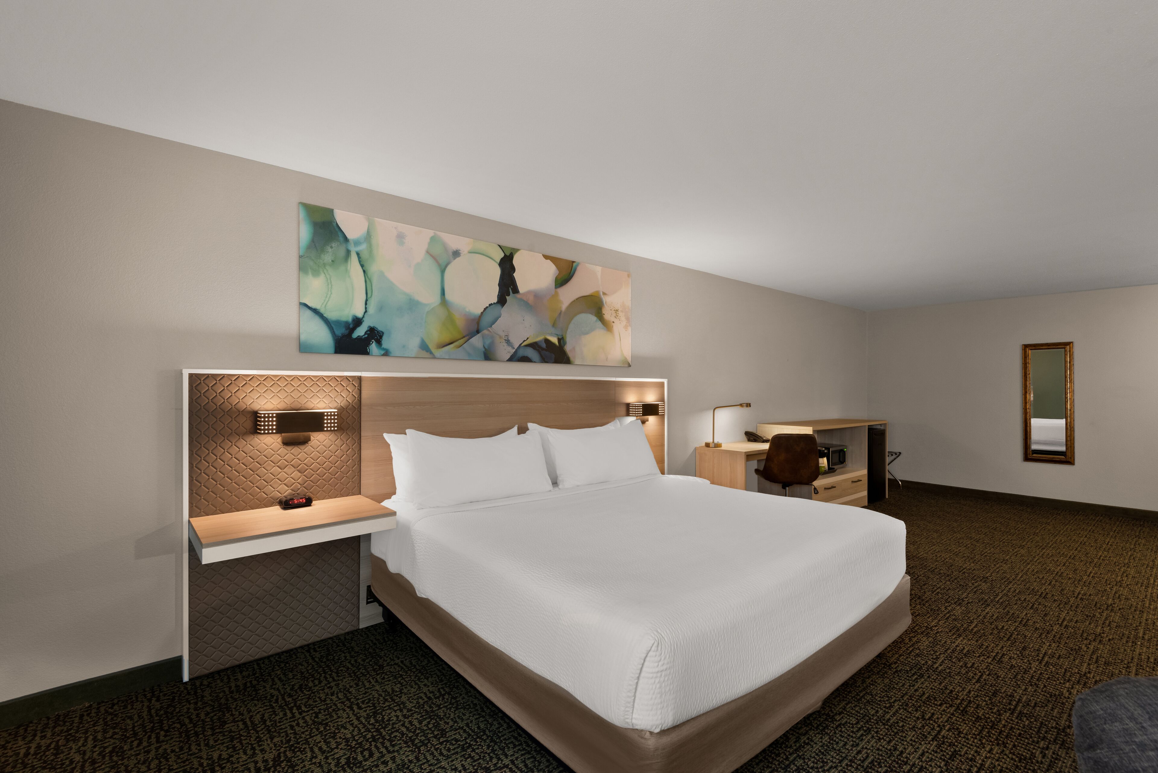 Habitación de hotel con una cama grande, un escritorio, una silla y una obra de arte en la pared.