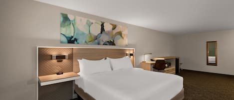 Habitación de hotel con una cama grande, un escritorio, una silla y una obra de arte en la pared.