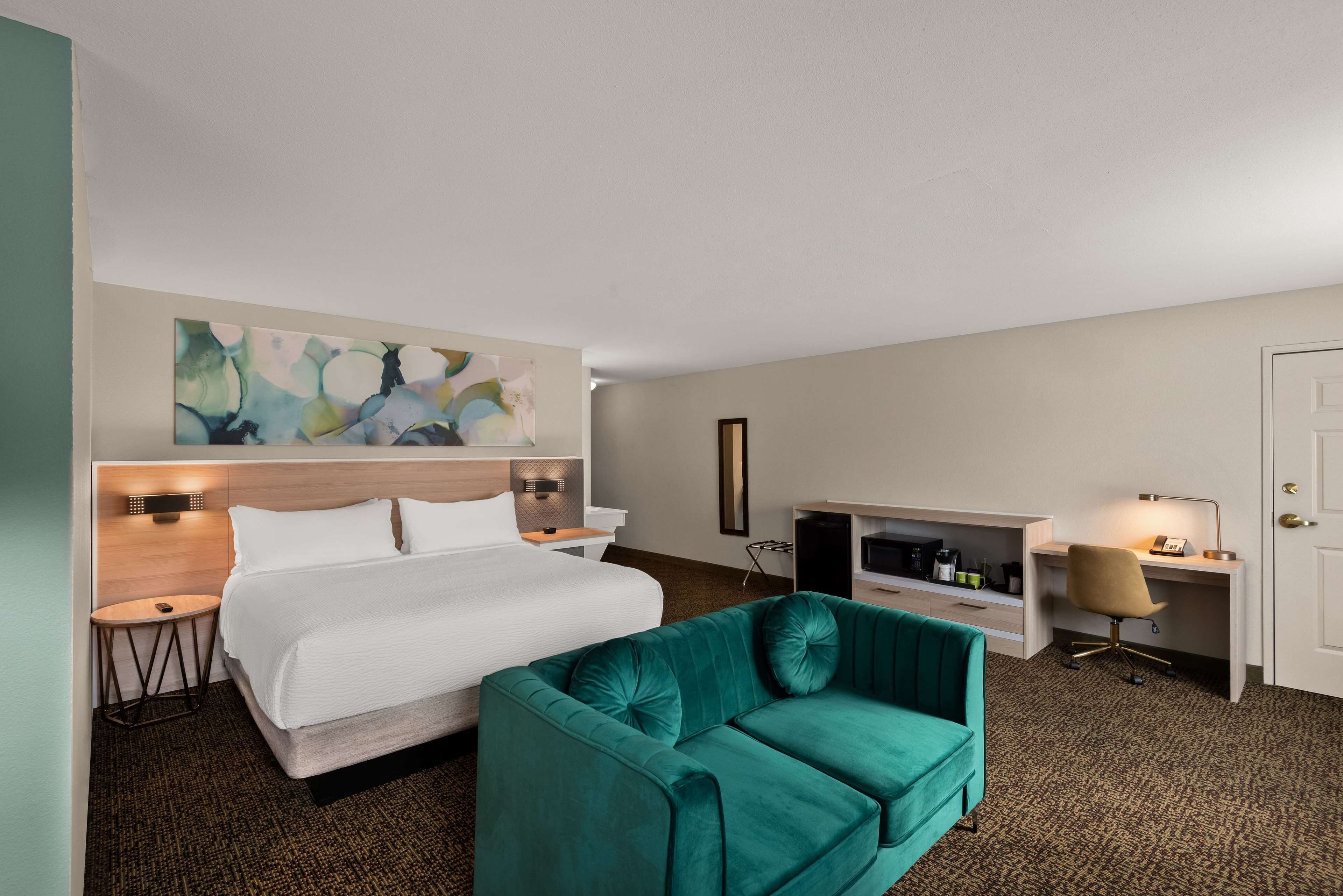 Ein Hotelzimmer mit Bett, Schreibtisch, Stuhl und einem großen abstrakten Gemälde an der Wand.
