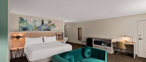 Ein Hotelzimmer mit Bett, Schreibtisch, Stuhl und einem großen abstrakten Gemälde an der Wand.