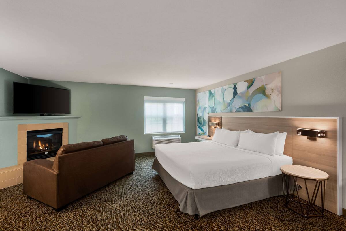 Una habitación de hotel con una cama grande, un sofá, un televisor de pantalla plana, chimenea y una ventana con persianas.