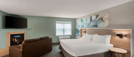 Hotelkamer met een groot bed, een bank, een flatscreen-tv, een open haard en een raam met zonwering.