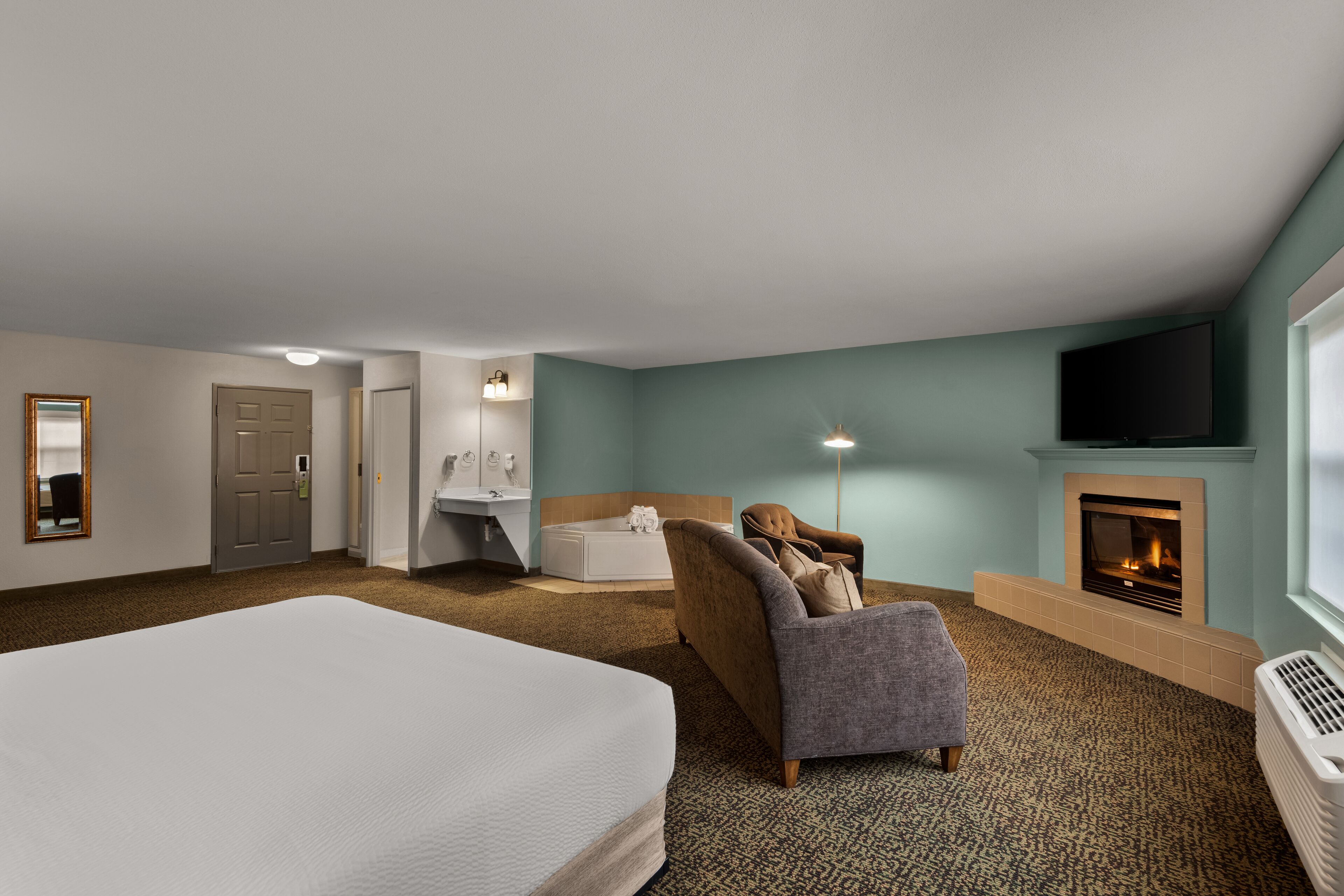 Ein Hotelzimmer mit einem großen Bett, einer Couch, einem Kamin, einem Fernseher und einem Badezimmer mit Spiegel und Waschbecken.