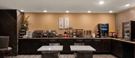Una cocina moderna con una isla central, taburetes de bar y una zona de estar con mesas y sillas.