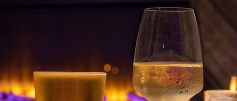 A glass of white wine and a tall glass of beer on a table with a candle and a plate of fries.