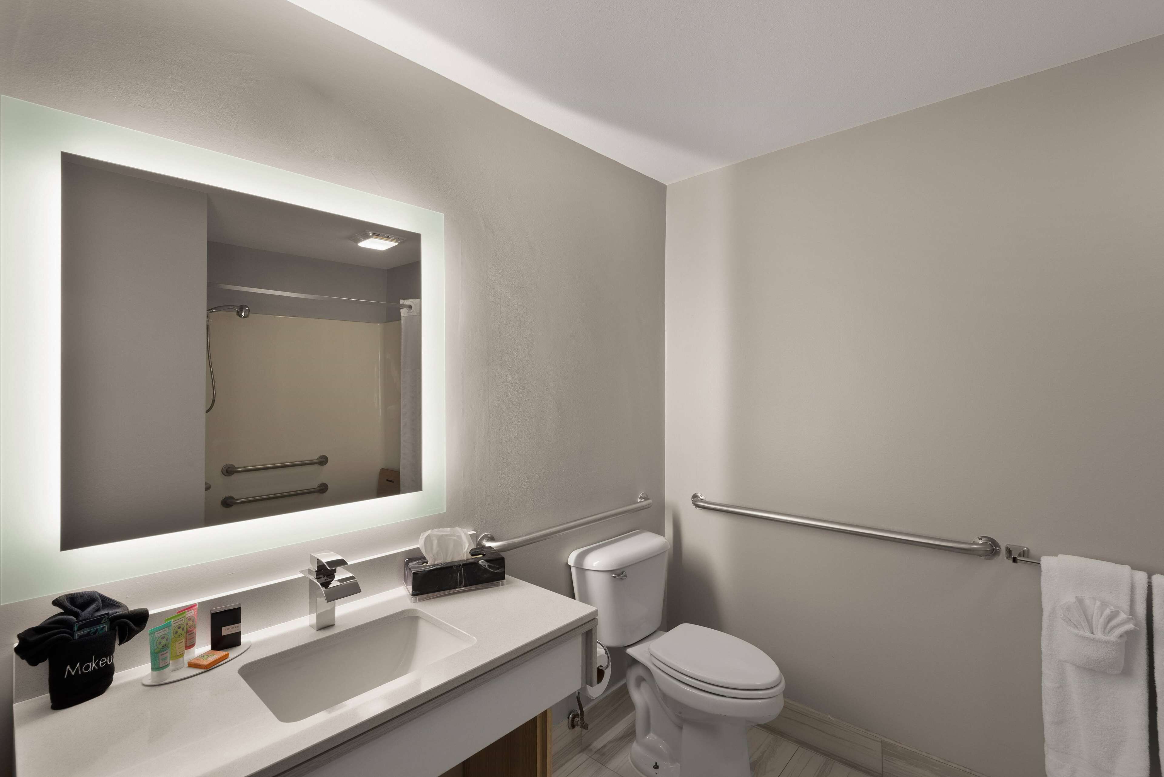 A modern bathroom with a large mirror, white sink, and toilet.