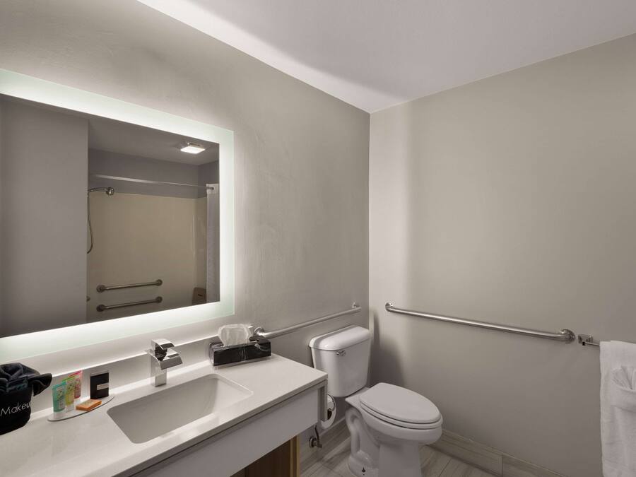 A modern bathroom with a large mirror, white sink, and toilet.