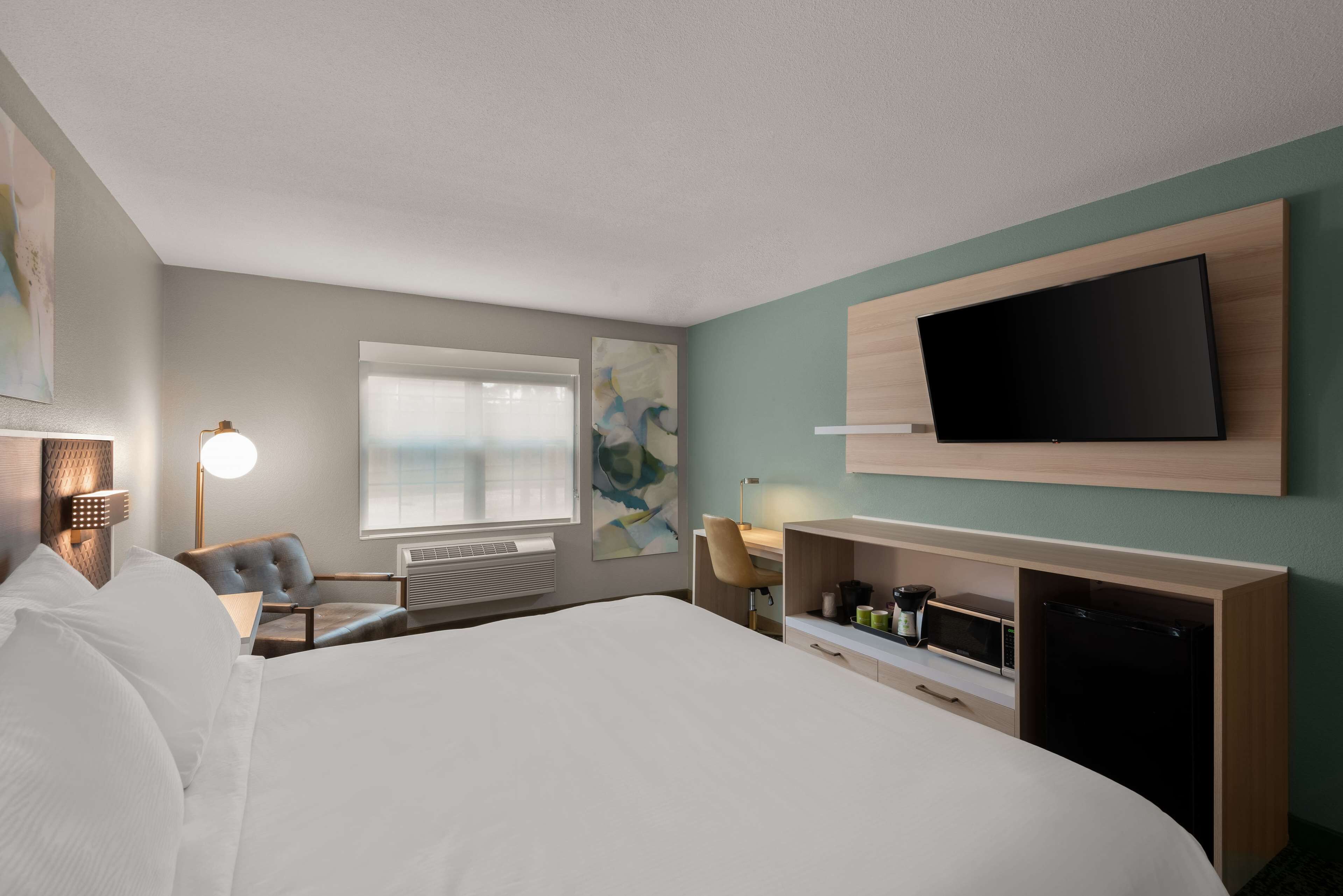 Een hotelkamer met een groot bed, een bureau met stoel, een flatscreen televisie aan de wand en een raam met jaloezieën.