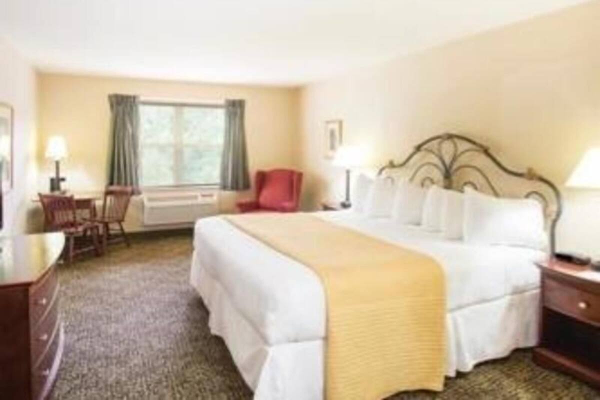 Una habitación de hotel con cama, escritorio, silla, ventana y mesita de noche.