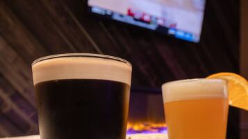 Deux verres de bière posés sur un dessous de verre, avec un téléviseur en arrière-plan.