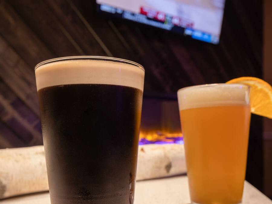 Two glasses of beer on a coaster, with a TV in the background.