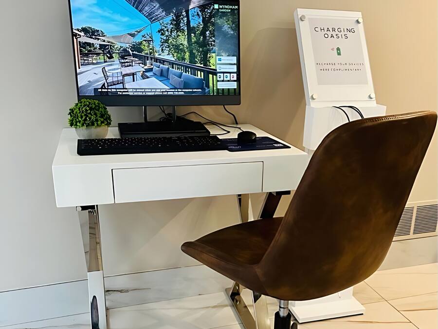 A modern office setup with a white desk, a computer monitor, a keyboard, a mouse, a brown office chair, and a charging station.