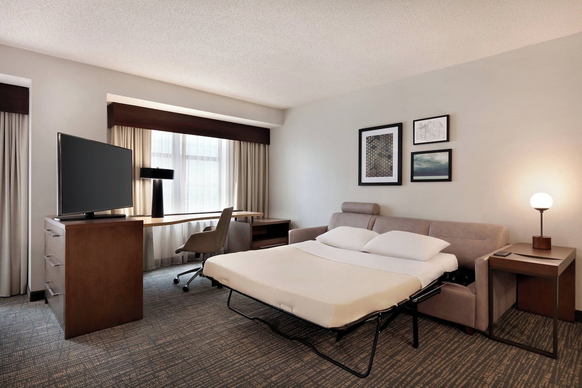 A hotel room with a bed, desk, chair, TV, and framed pictures on the wall.